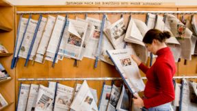 Student looks at a copy in front of a wall of newspapers.